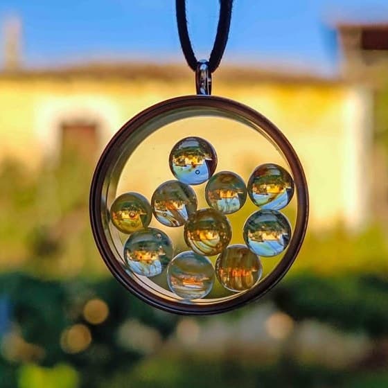 Handmade glass marble locket necklace held in golden-hour light, tiny borosilicate marbles catching the sun