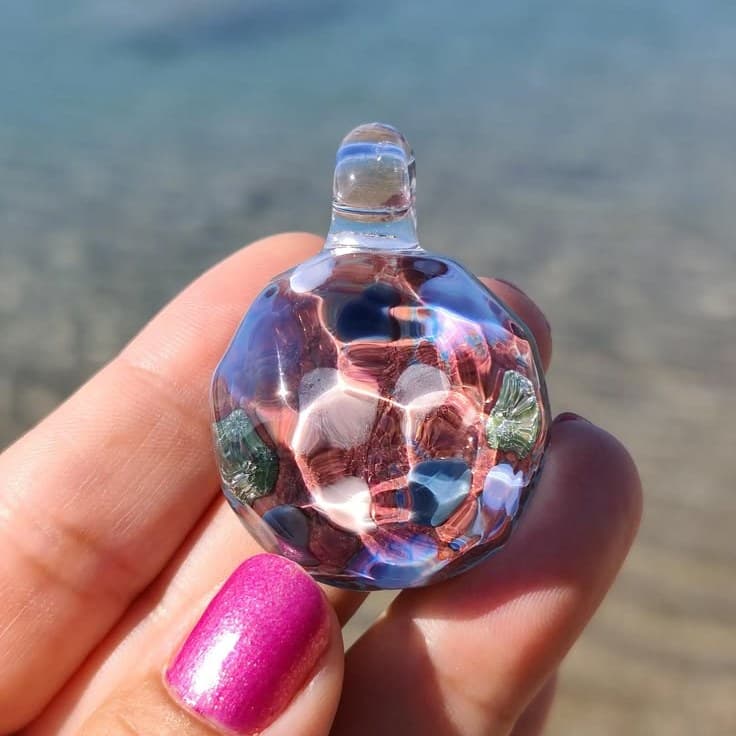 One-of-a-kind handmade galaxy glass pendant held in hand above the clear Aegean sea in Akrata, Greece