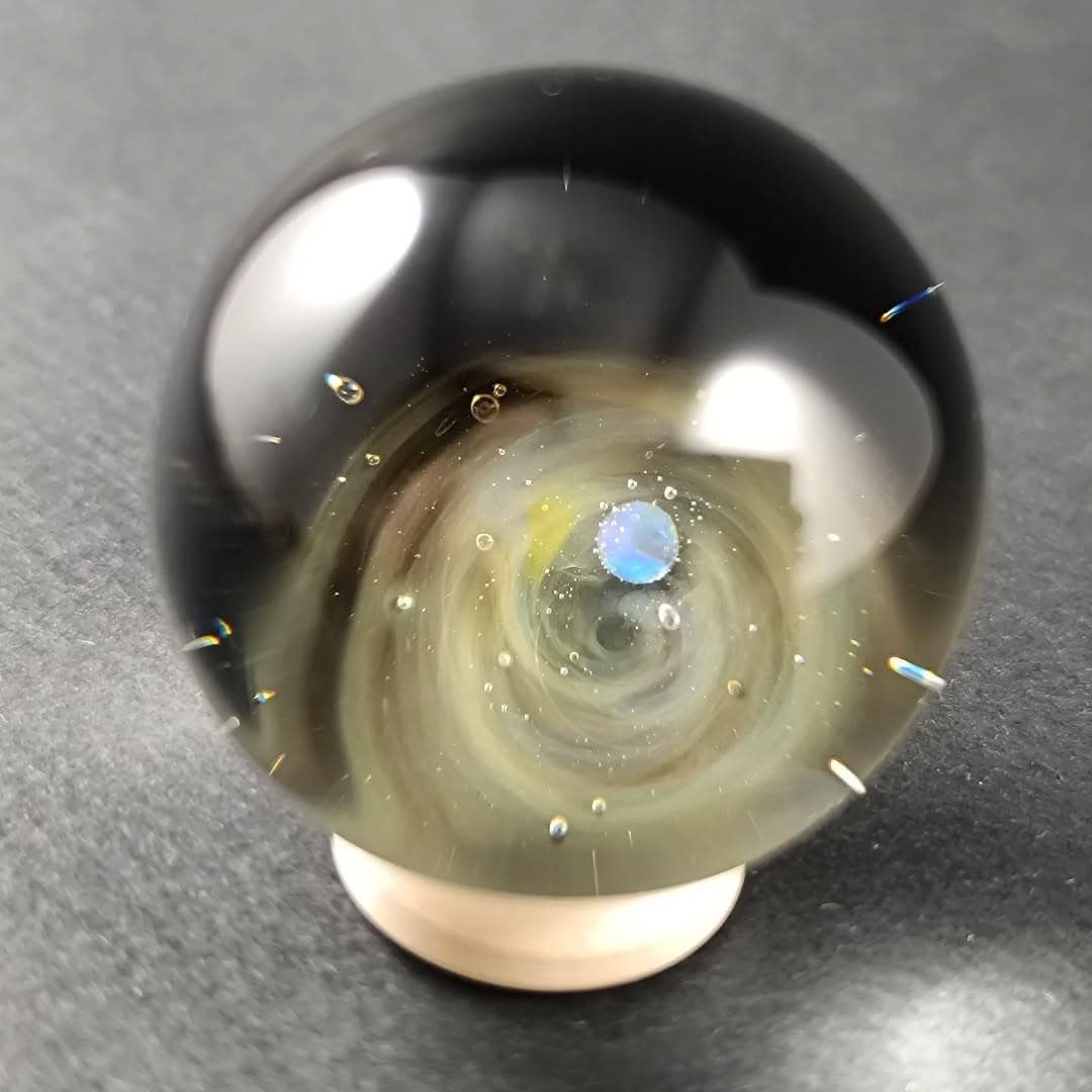 Silver-fumed galaxy glass marble with a glowing opal planet over a swirling nebula — a collectible handmade borosilicate sphere