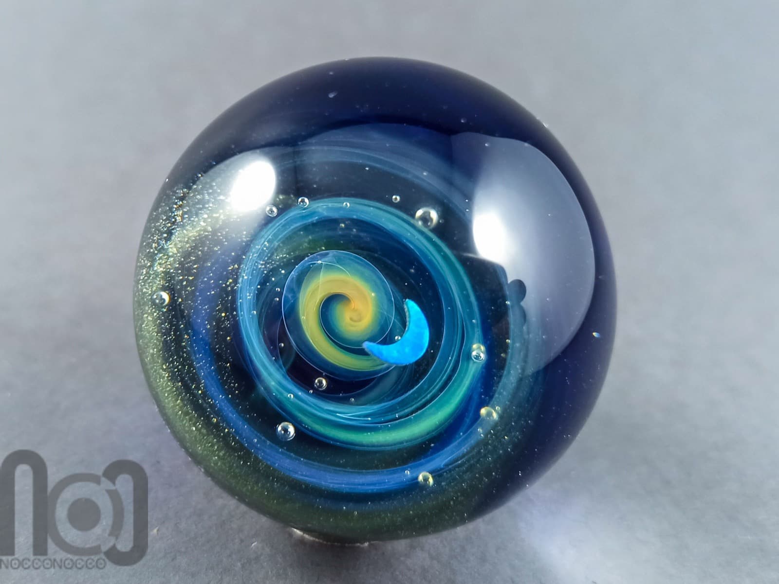 A galaxy glass marble held to the light in the studio