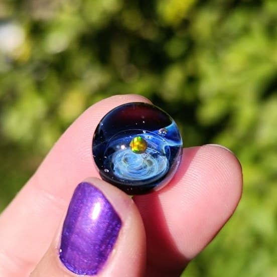 Silver-fumed galaxy glass marble with a floating opal planet, held in hand in the Greek sunlight