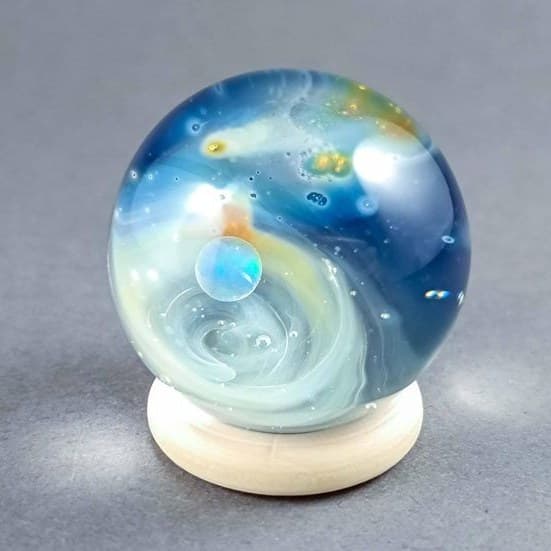 Handmade space glass marble with an opal planet suspended over a swirling nebula